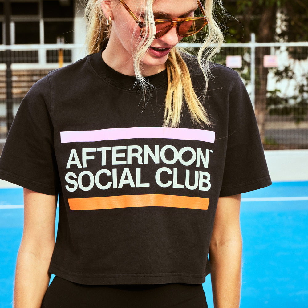 Female model wearing black crop top Afternoon Social Club featuring brand name and colours 