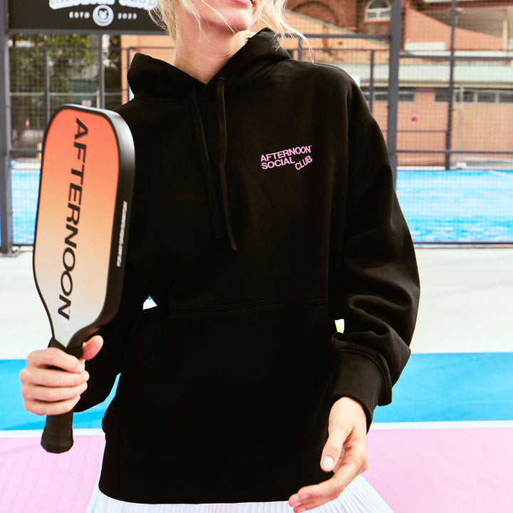 Female Model wearing a black Afternoon Social Club Heavy hoodie with oversized fit and a carbon fiber pickleball paddle