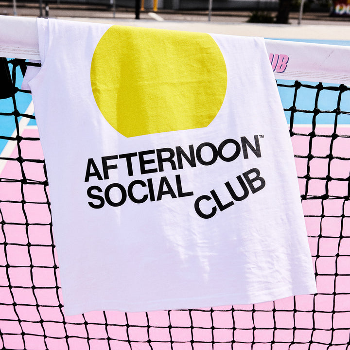 White tank top with yellow sunset circle and Afternoon Social Club lettering on pickleball net