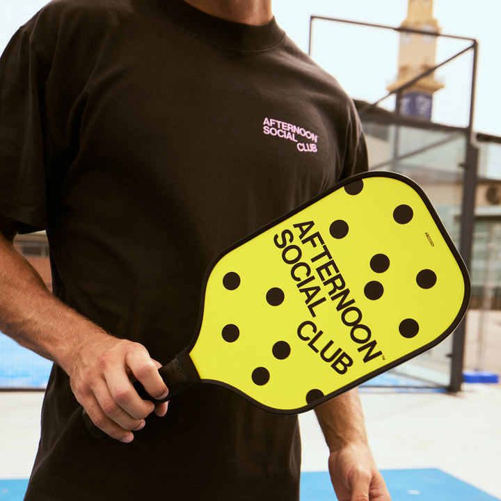 Male holding Yellow carbon Fiber Pickleball paddle with dots and afternoon social club logo