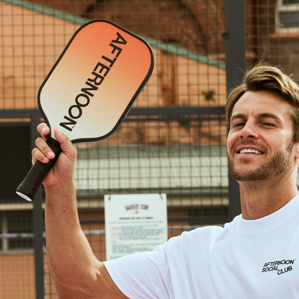 male model holding an afternoon social club carbon fiber pickleball paddle with an orange gradient and words afternoon on it