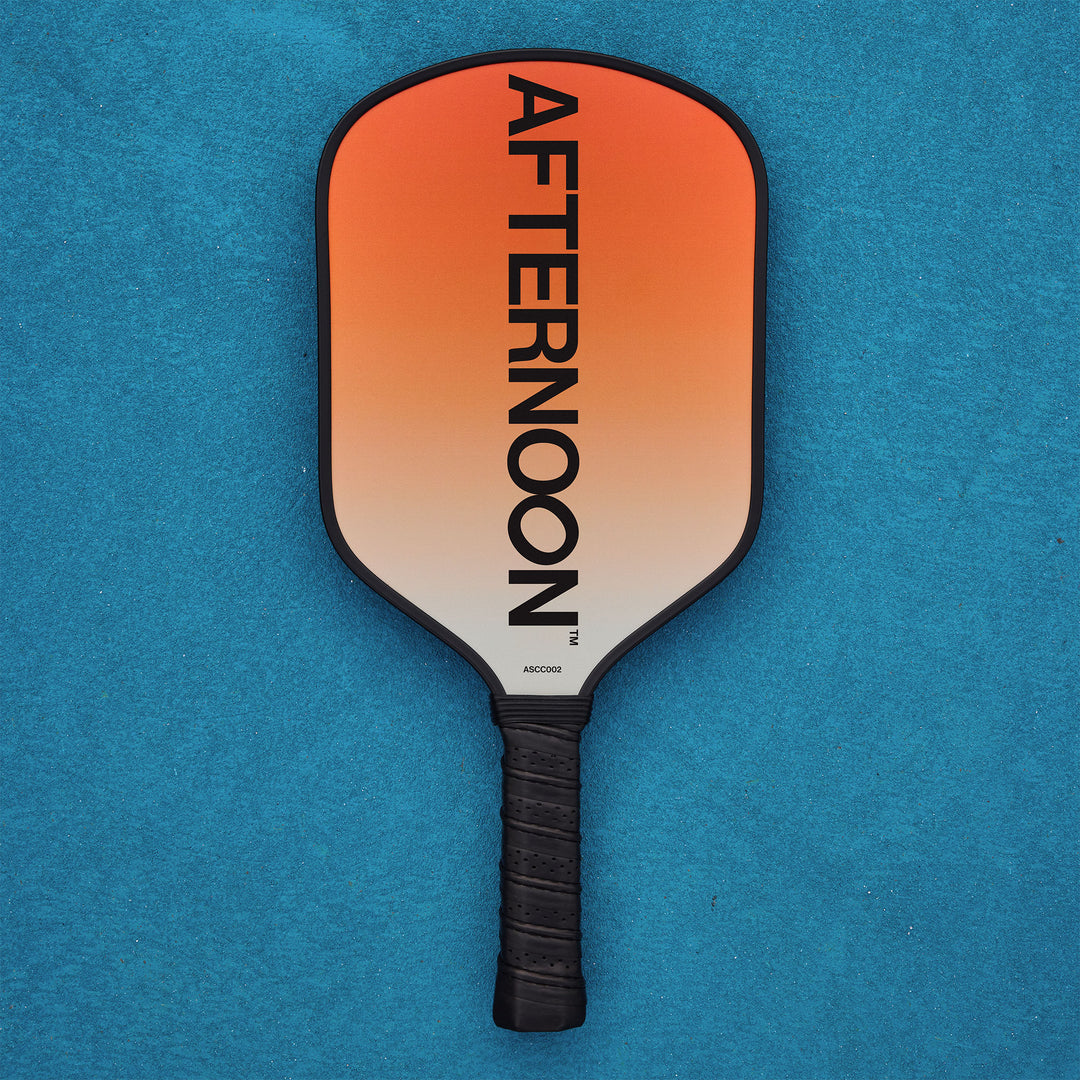 An afternoon social club carbon fiber pickleball paddle with an orange gradient and words afternoon on it