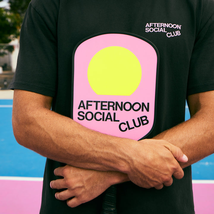 Male Model on the pickleball court holding Pink Fiberglass Pickleball Paddle featuring Afternoon Social Club logo and yellow sun