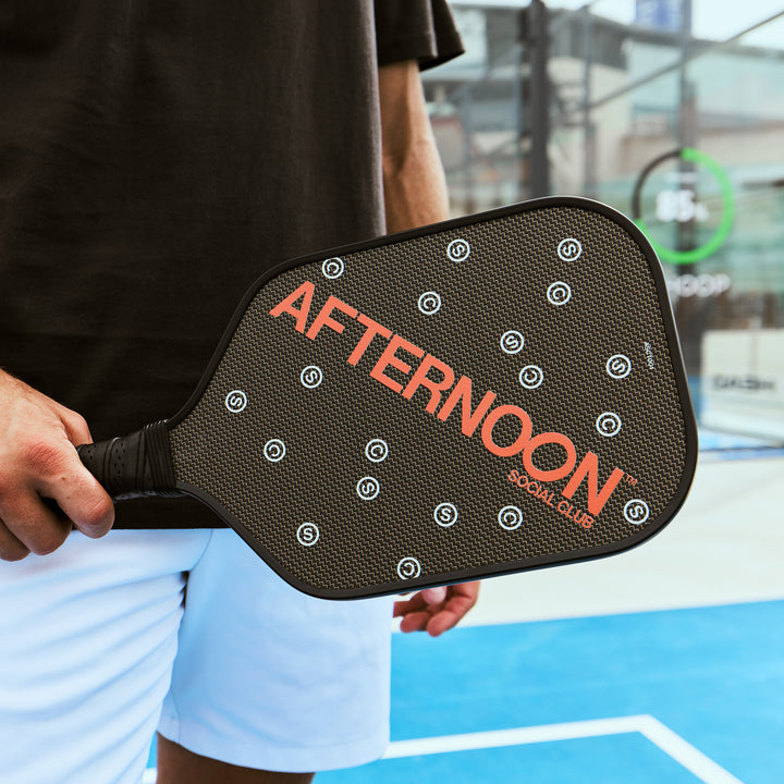 male holding black titan carbon pickleball paddle featuring the words Afternoon SC in orange and white 