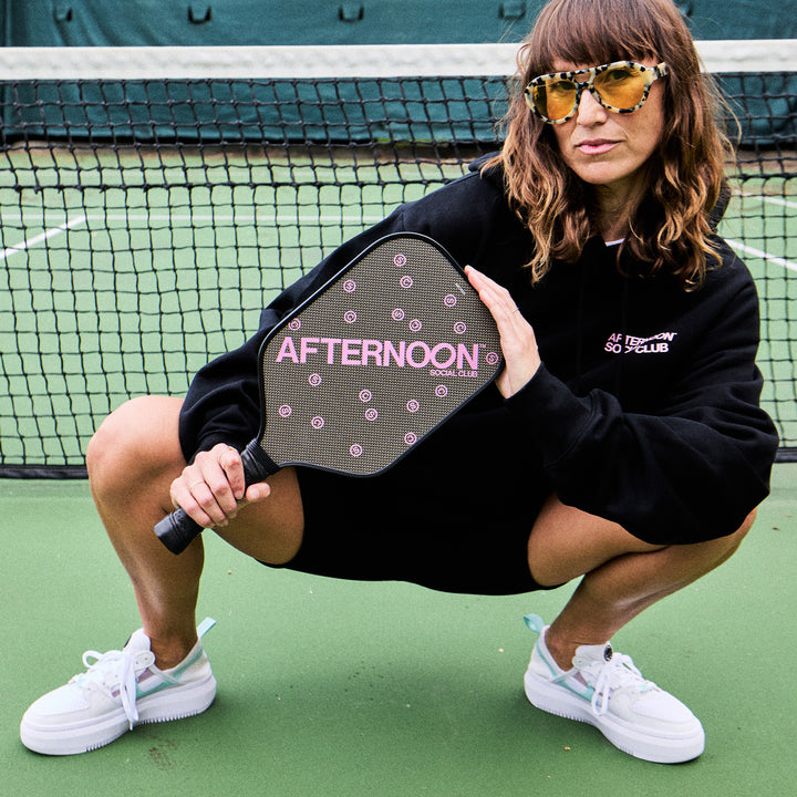 A female posing and holding a black titan carbon pickleball paddle with the words Afternoon SC in purple