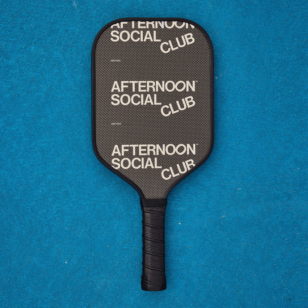 A black titan carbon pickleball paddle with the afternoon social club logo repeated