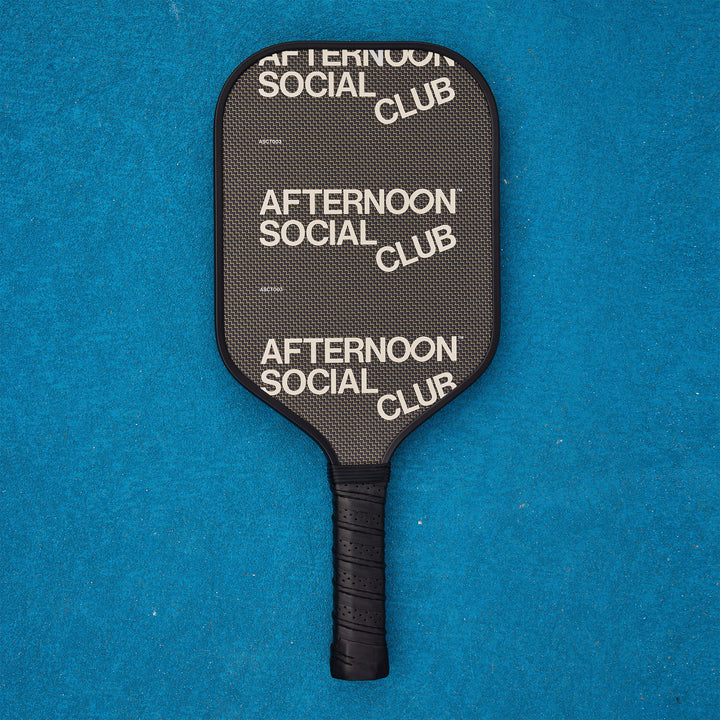 A black titan carbon pickleball paddle with the afternoon social club logo repeated